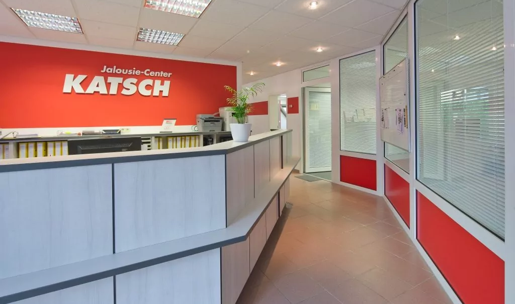 Der Eingangsbereich des Jalousie-Center Katsch mit Tresen und großem Logo mit roten Akzenten im Raum.