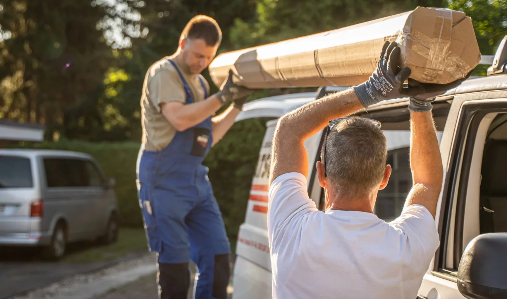Zwei Mitarbeiter des Jalousie-Center Katsch heben ein verpacktes Teil des Sonnenschutzes vom Dach des Firmenwagens.