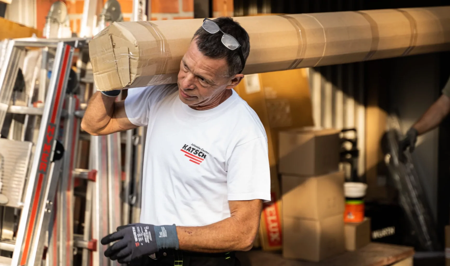Mitarbeiter des Jalousie-Center Katsch trägt ein Sonnenschutz-Bauteil aus dem Lager.