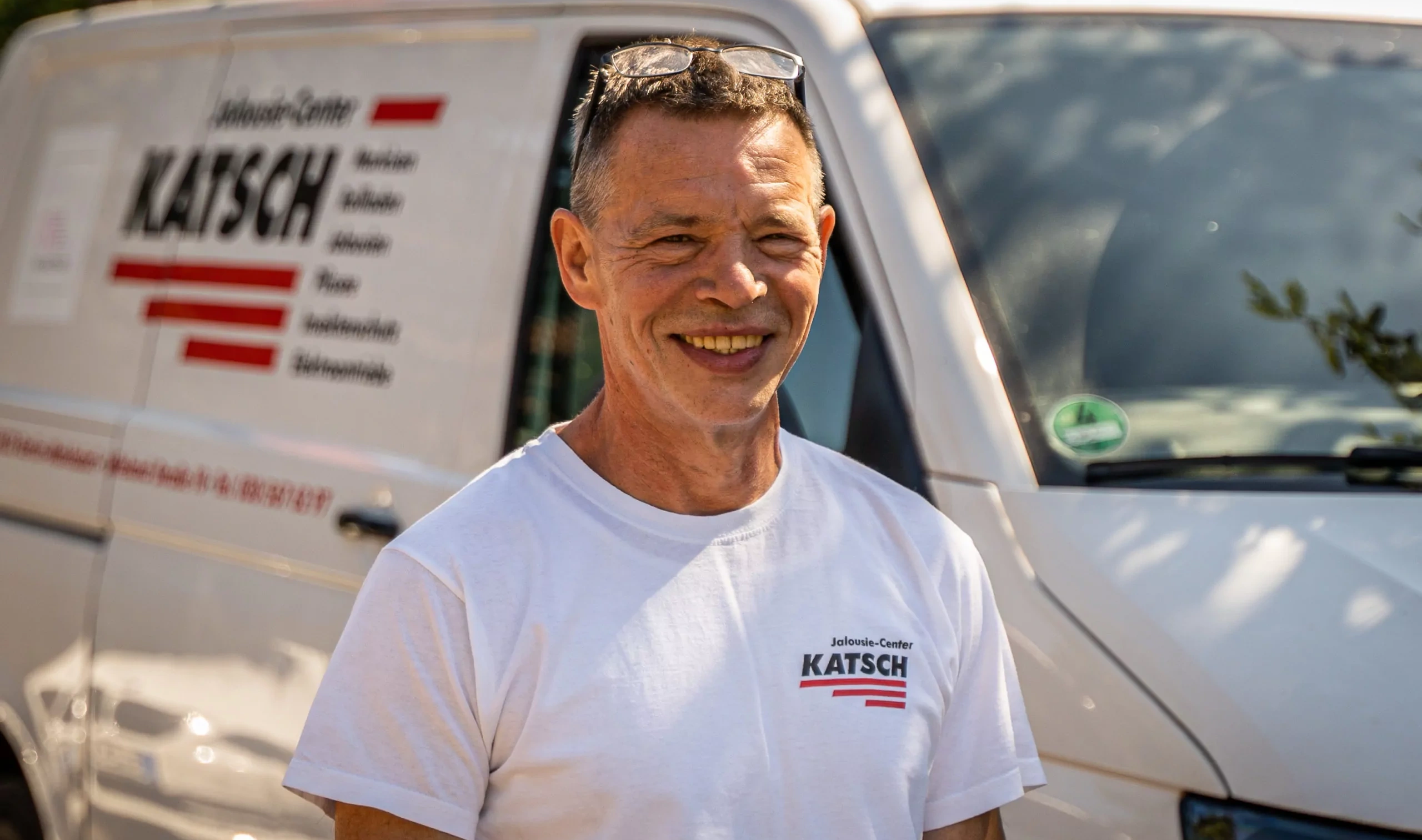 Lächelnder Mitarbeiter des Jalousie-Center Katsch vor dem Firmenwagen des Unternehmens.